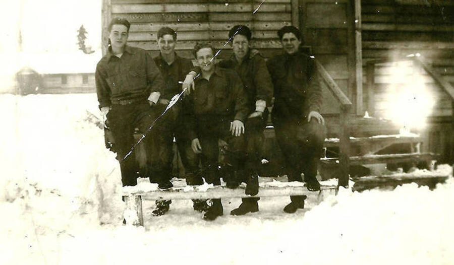 Five CCC men pose in front of their barrack at CCC Camp Big Creek #2, F-132. Snow covers the ground. Back of the photo reads: 'Winter of 38/39'.