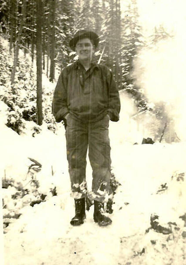 A CCC man poses in the snowy woods near CCC Camp Big Creek #2, F-132. Back of the photo reads: 'Can't remember name - good guy in my barracks'.