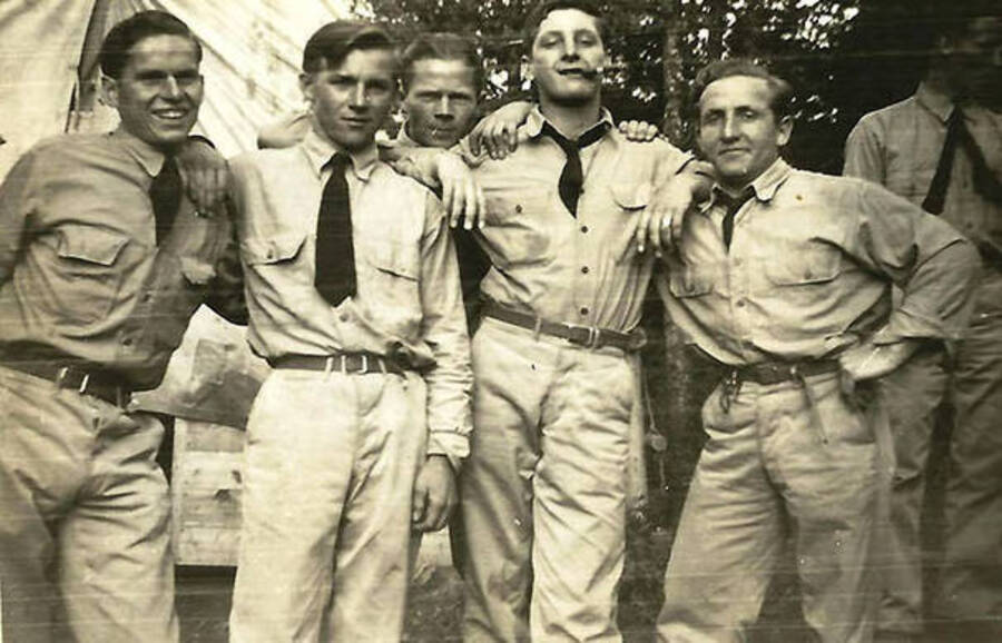 Five CCC men pose in front of a tent barrack at CCC Camp Big Creek #2, F-132. One of them is smoking a cigar and another is chewing on a toothpick.