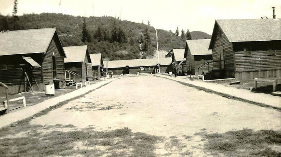 A view down the middle of the barracks with the headquarters building in the background at CCC Camp Big Creek #2, F-132. Back of the photo reads: 'Company Street - looking toward Hqtrs building CCC Co. 531'.
