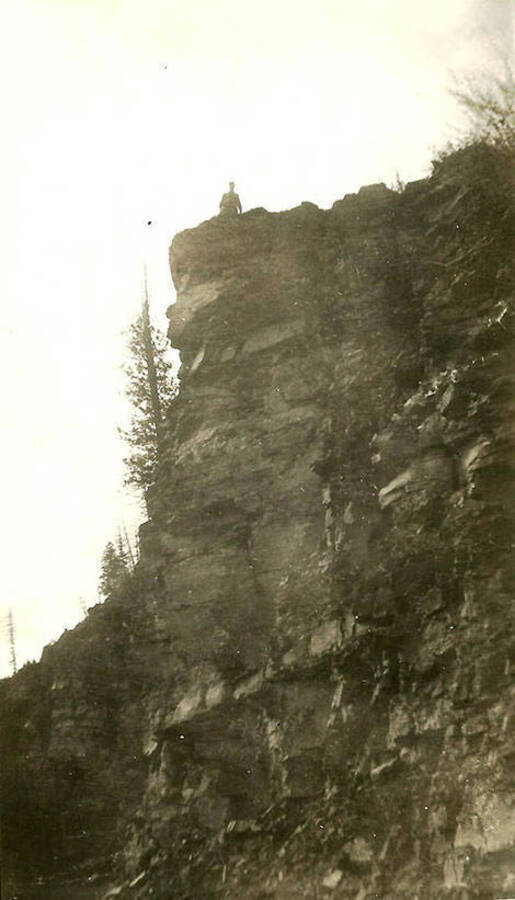 A CCC man looks down from the top of a cliff near CCC Camp Big Creek #2, F-132.