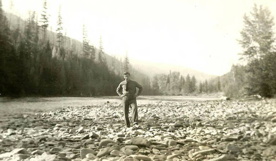 A CCC man stands on the rocky bank of a creek near CCC Camp Big Creek #2, F-132. Back of the photo reads: 'Dry river bed until spring floods.'