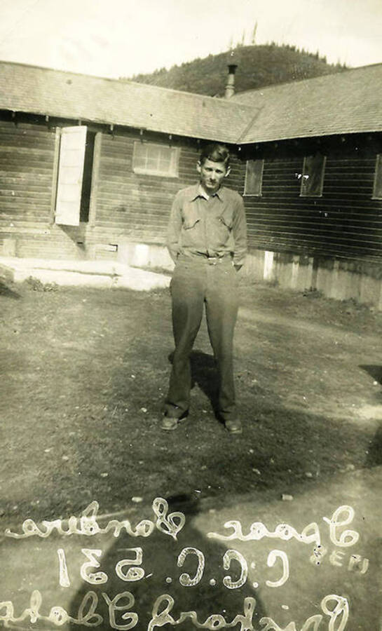 A CCC man stands in CCC Camp Big Camp #2, F-132. There is writing on the photo that can be read in reverse. It reads: 'Isaac Sanders CCC 531 Prichard, Idaho'
