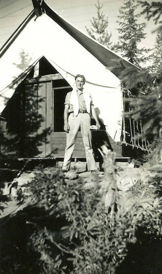 A CCC man stands in front of a tent barrack at the spike camp in Mullan, Idaho. Back of the photo reads: 'Spike Camp'