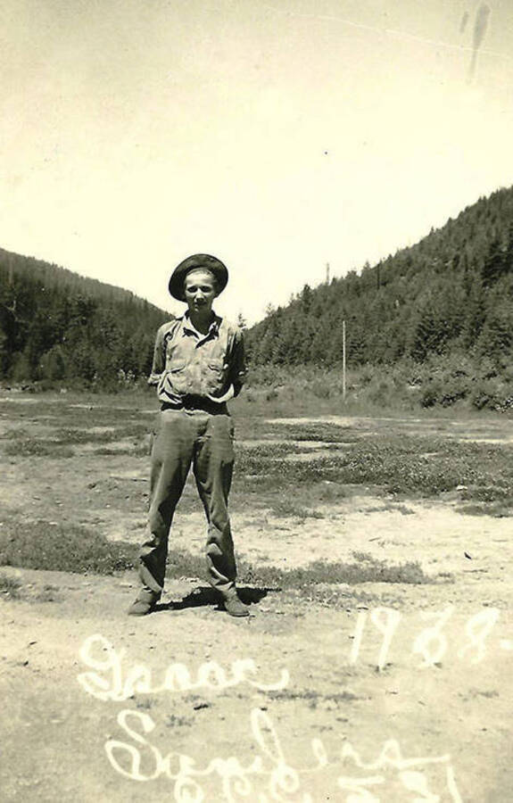 A CCC man stands at parade rest in a field near CCC Camp big Creek #2, F-132. Writing on the photo reads: 'Isaac Sanders 1938 CCC 531.'