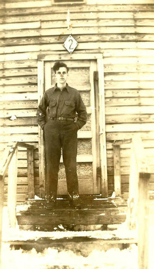 A CCC man stands in front of the Barracks at CCC Camp Big Creek #2, F-132. Snow covers the bottom step. Back of the photo reads: 'Winter '38/'39 CCC Co. 531'.