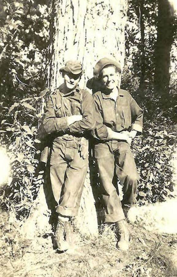 Two CCC men leaning against a tree in the woods near CCC Big Creek Camp #2, F-132. Back of the photo reads: 'Taking a break from Blister-rust work'.