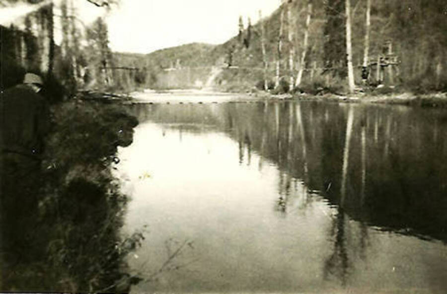 A view of the North Fork of the Coeur d'Alene River and the water pipeline that leads to CCC Camp Big Creek #2, F-132. Back of the photo reads: 'View of the river showing the water pipe line bridge in the background. Taken 1938'.