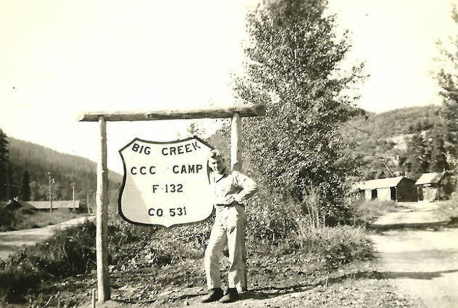 A CCC man stands in front of the sing for CCC Camp Big Creek #2, F-132. The sign reads: 'Big Creek CCC Camp F-132 Co. 531' Back of the photo reads: 'Big Fred Sokant (from W. Va) holding up the sign.'