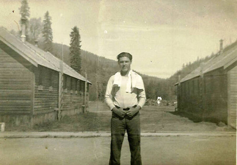 A CCC Man poses in-between two barracks with a towel around his neck. Photo taken at CCC Camp Big Creek, F-132.