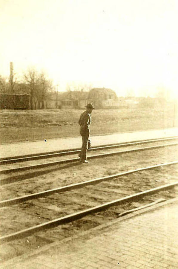 A CCC man stands on the railroad tracks with houses in the background.