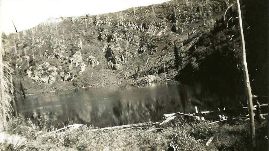 A lake in the middle of a snag-covered crater. Back of the photo reads: 'One of the 'twin' lakes above the Shoshone County Park. Near where Hi-way 90 crosses Mullan Pass into Montana.'