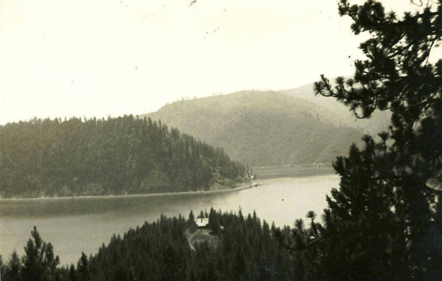 A photo of a House perched on a hill above the lake. It appears one of the hills rises from the lake and may in fact be an island.