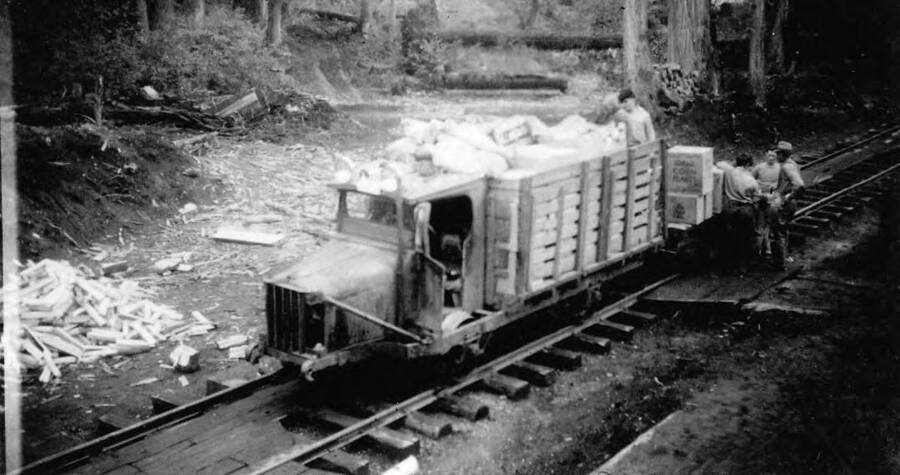 A photo of a delivery truck on the train tracks being loaded to deliver camp supplies the  CCC camps near Headquarters, Idaho. 'Kellogg's Corn Flakes' can be seen written on some of the boxes.