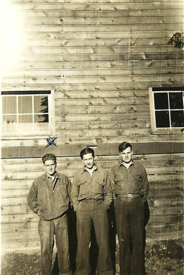 Three CCC men pose against the side of a building at CCC Camp big Creek #2, F-132. Back of the photo reads: 'John, I am under the x with a couple of friends, ready for week-end duty in camp. X=John E. Platt Berghalz, Ohio'.