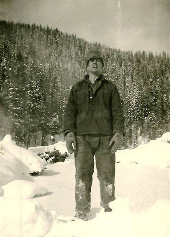 A CCC man stands outside CCC Camp Big Creek #2, F-132, in the snow a forested hill behind him. Back of the photo reads: 'George Bugai?? From near Tiltonsville, Ohio.