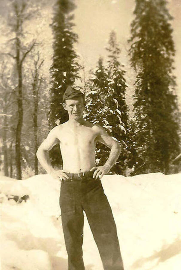 A CCC man stands shirtless in the snow-covered forest. Back of the photo reads: 'Boy I'm tough!'