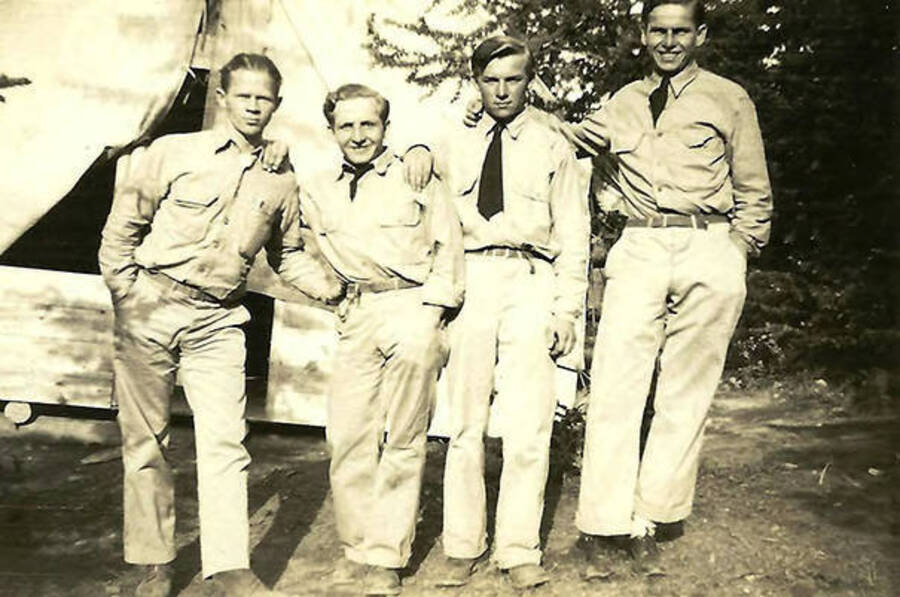 Four CCC men pose outside of a tent barrack at the Mullan, Idaho spike camp. Back of the photo reads: 'On right Ed Sash 2nd from right Elya Burge from Rayland, Ohio below Steubenville. Can't remember others.'