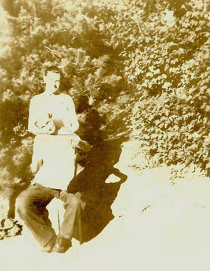 Two CCC men posed for a photo, one in a chair with a towel over his chest, the other standing behind him. Back of the photo reads: 'Getting' a haircut'