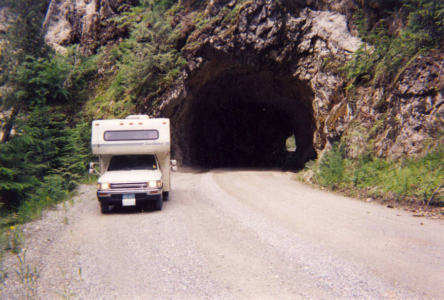 An RV is parked in front of the Fishhook Creek Tunnel, South of Avery, ID on Fishhook Creek. The back of the photo reads: ''Fishhook Creek Tunnel' Built by CCC 1938-1939. Visited July 1999 by Herb VanKirk and CCC + T.V. Crew from Public T.V. 'Outdoor Idaho' from Boise, Idaho.'