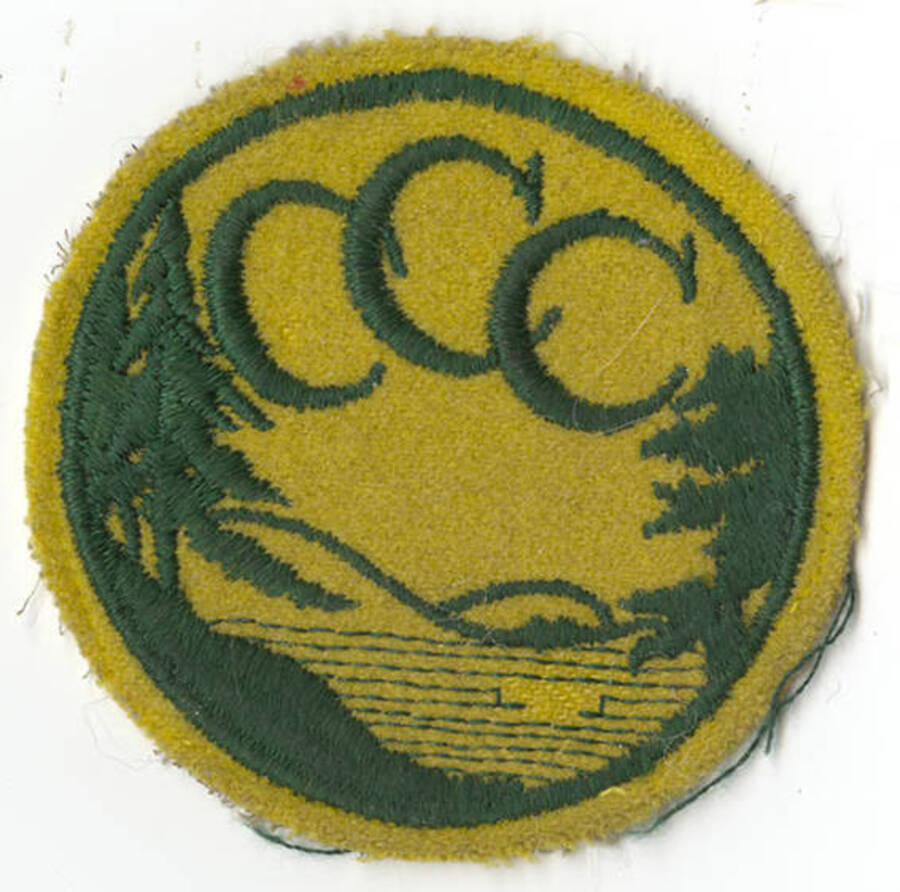 A scan of a CCC patch donated by Douglas Eier. The patch depicts a lakeshore with trees in the foreground and hills in the background, with three inter-lacing Cs at the top of the patch.