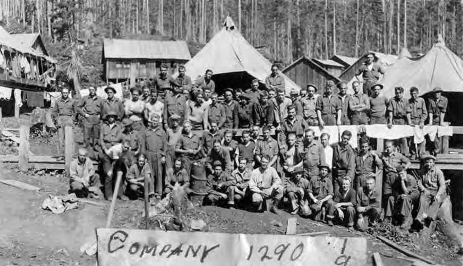 Company photo in a CCC camp. The men are standing in front of various tents and buildings. Most of the men are in uniform, while a few are shirtless. Writing under the photo reads: 'Company 1290 CCC Idaho 1933'.