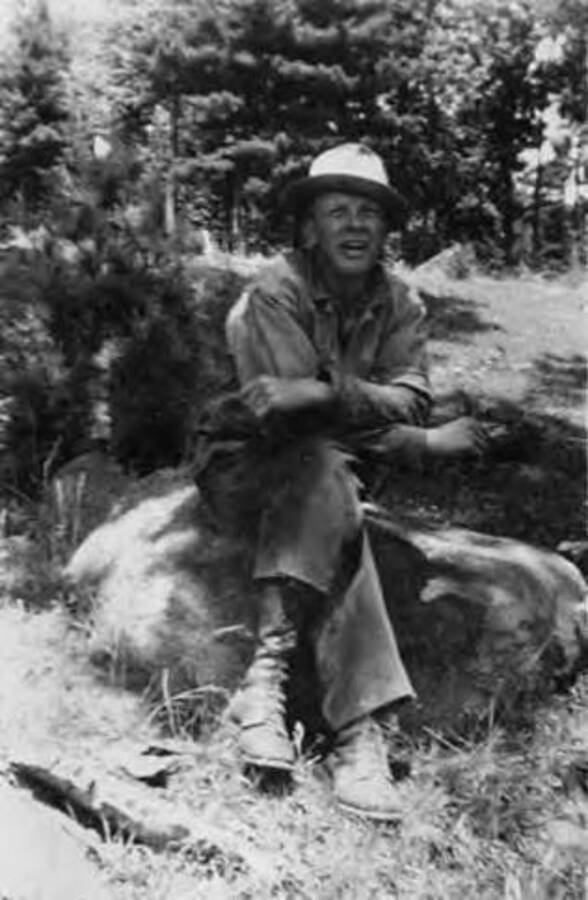 A CCC man sitting on a rock in the woods.