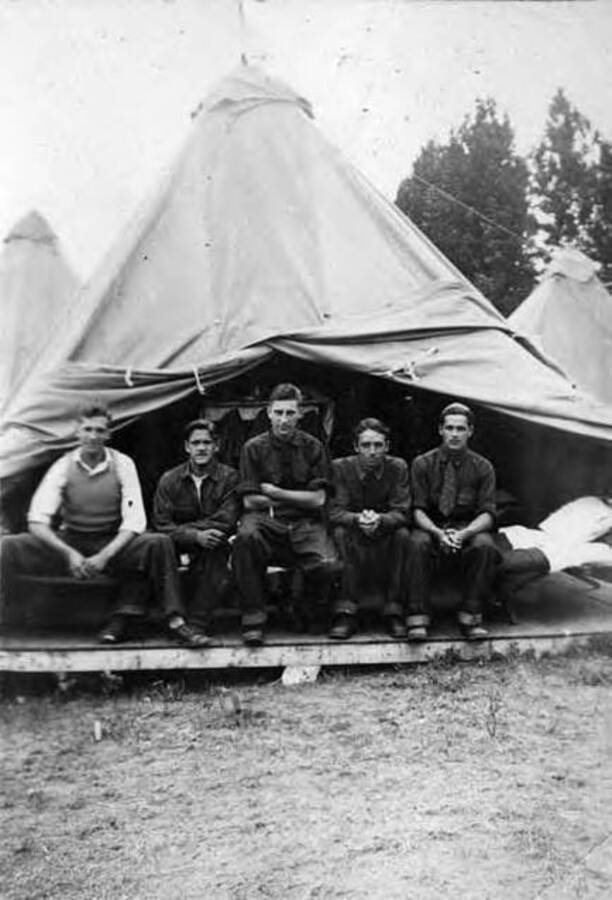 Five CCC men sitting on the bunk underneath a tent. Writing under the photo reads: 'Platsburg'.