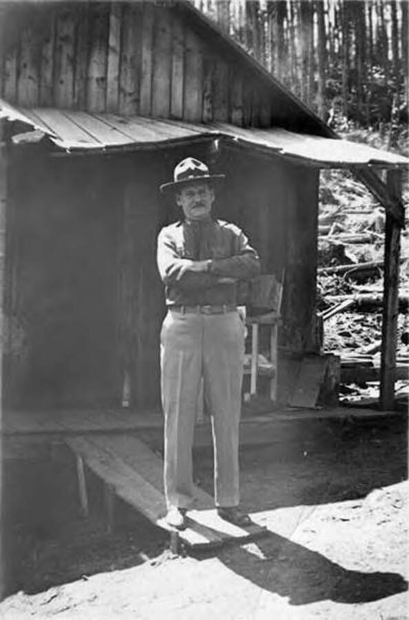 A CCC man stands on a ramp in front of a building. Writing on the photo reads: 'John E. Creed' Writing below the photo reads: 'John E Creed Co. Commander'.