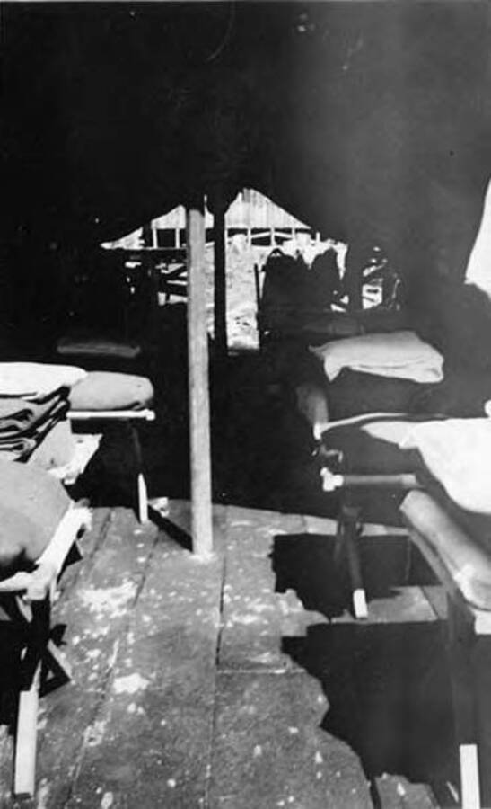 An interior view of a tent in a CCC camp. There are at least six cots in the tent with folded blankets on the end. Writing under the photo reads: 'Inside Tent 3 Idaho'