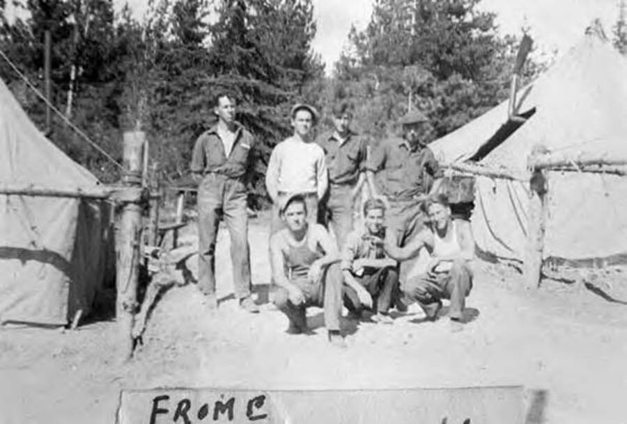 Seven CCC men posing outside two tents in a CCC Camp. Writing under the photo reads: 'From C Whitehall'