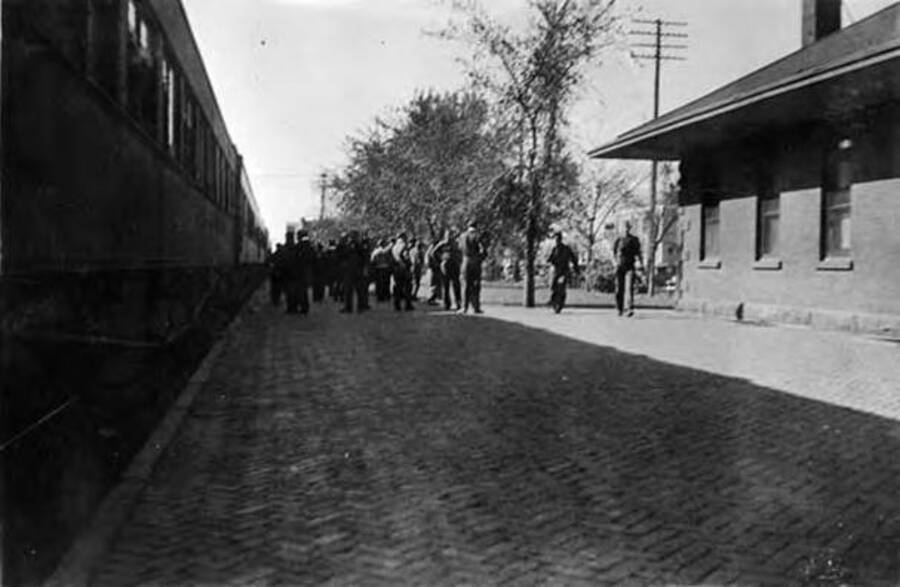 Several CCC men loitering around a railroad station. Writing below the photo reads: 'Rock Springs Wyoming'.