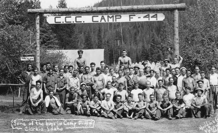 Group portrait of some of the men stationed at Camp F-44 near Clarkia, Idaho. Sign reads 'CCC Camp F-44' and the small sign to the left says 'Fire Alarm'.