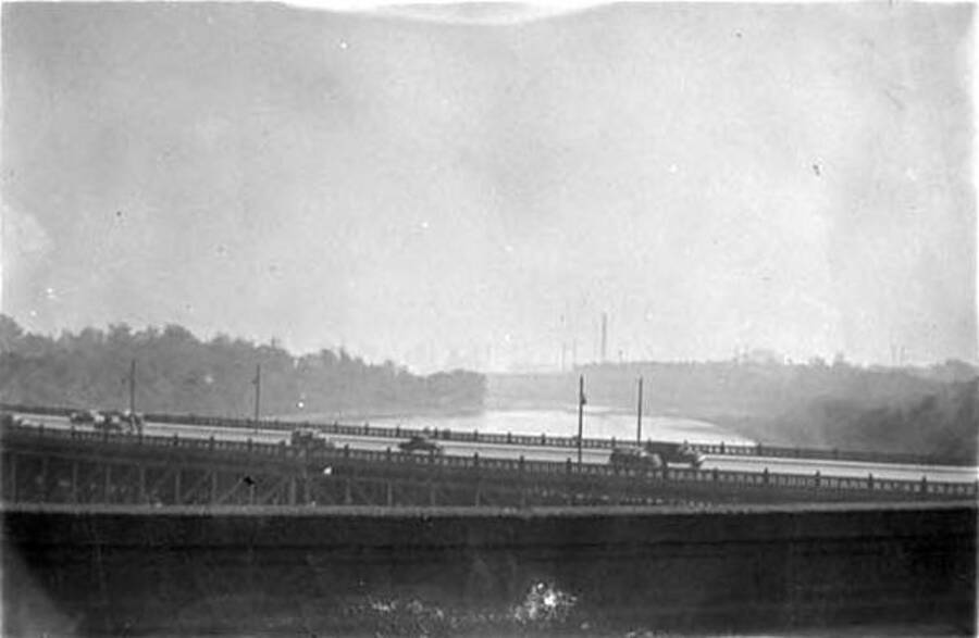 A photo of several automobiles crossing over a river, via a bridge, in Philadelphia, Pennsylvania. The city can be seen through a layer of fog in the background. Writing below the photo reads: 'Phildelphia'.