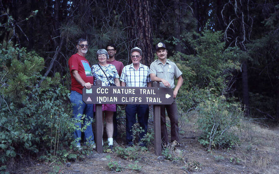 Five people standing behind a sign for the Indian Cliffs trailhead. One of the men is wearing a forest ranger's uniform. The sign reads: 'CCC Nature Trail, Indian Cliffs Trail'.