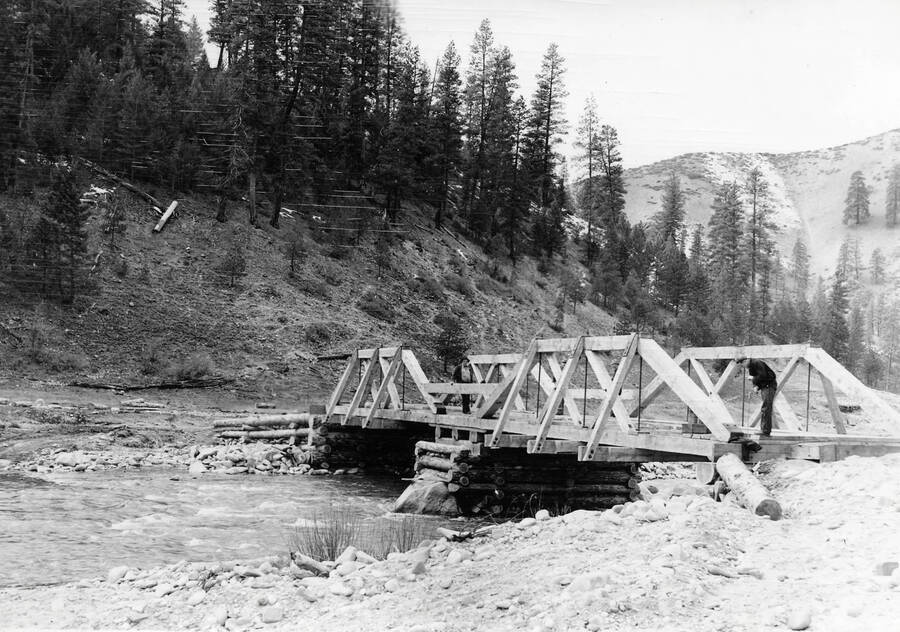 Two men working on a bridge across a small creek.