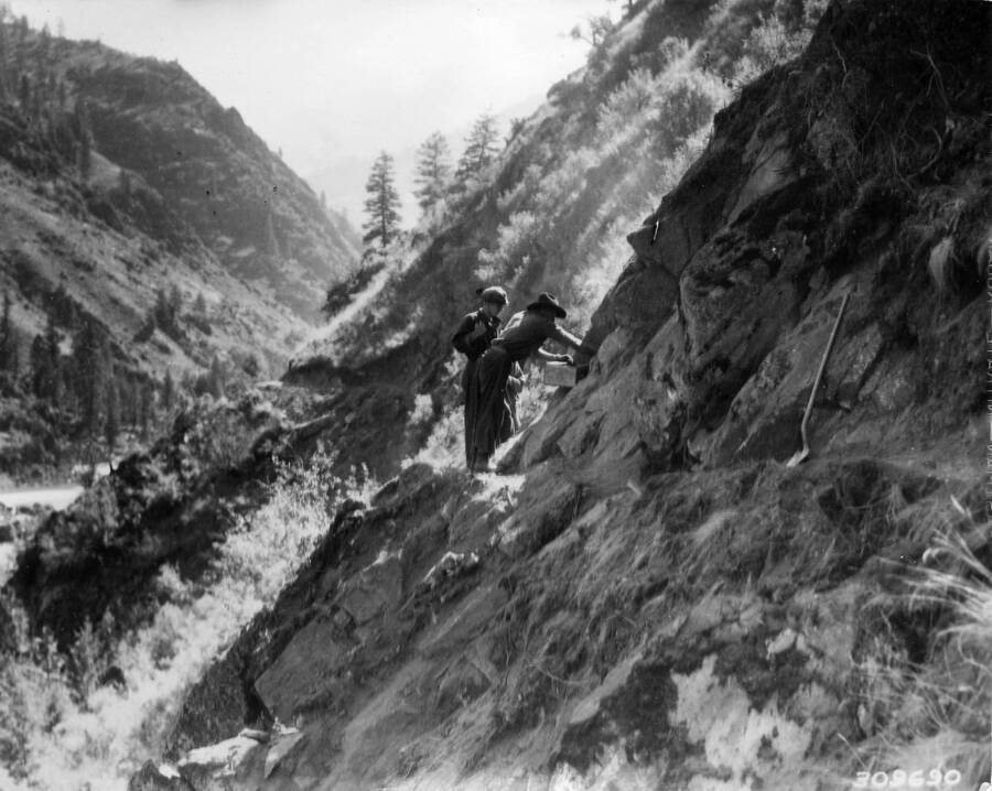 Two CCC Men working on the Salmon River road project on the cliff face above the river.