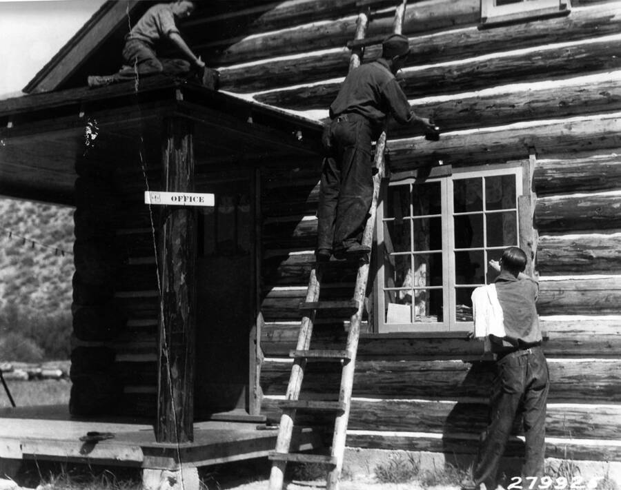 Three CCC men from Redfish Lake Camp painting a Guard Station, Challis National Forest. Taken in August. Sign reads: 'Office'. Back of photo reads: 'Idaho Boys from Redfish Lake Camp painting [Skakim] Challis National Forest August 1937.'