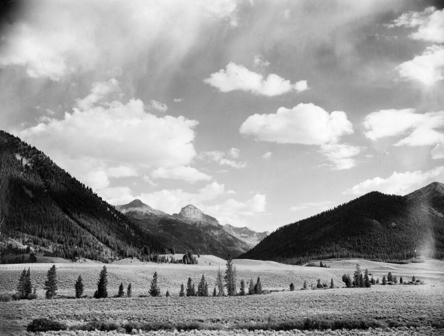 A mountain is visible across a valley and between two hills. Description reads: 'Hyndman Peak (12,078 ft. elevation) as seen from upper Big Lost River near Kane Creek on Forest Road to Ketchum. Forest: Challis, State: Idaho, Date: 7/1940, Author: P.S. Bieler'.