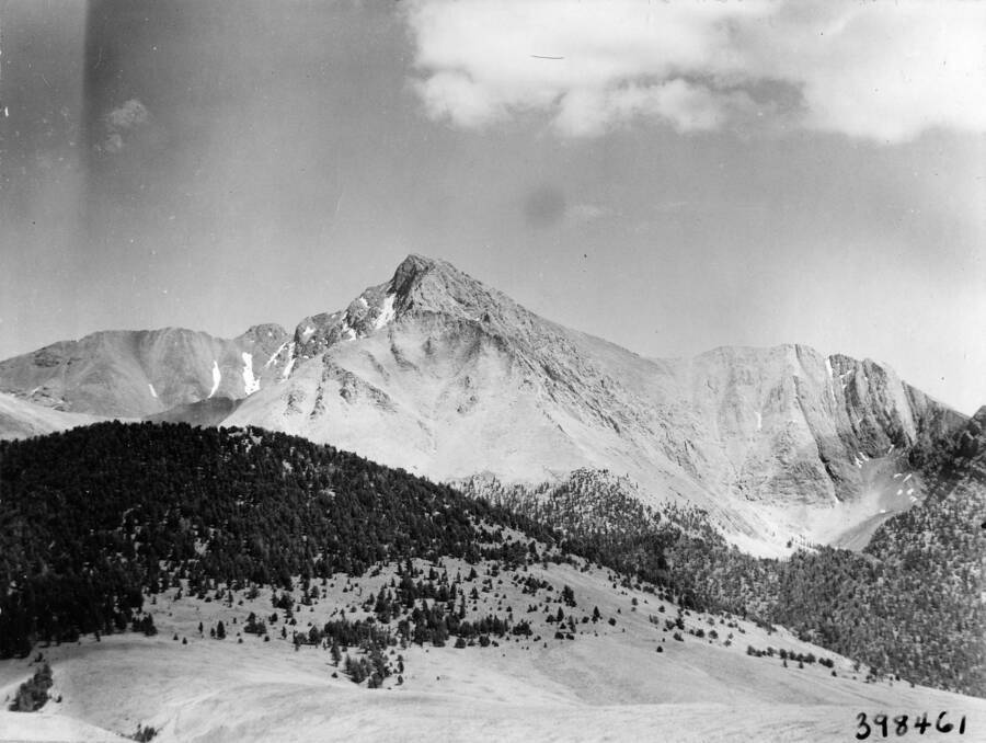 A mountain rises above some wooded foothills. Description reads: 'Telephoto view of Mt. Borah (12,655 ft. elevation) highest mountain in Idaho, taken from Grazing Service CCC Camp Chilly #111. Forest: Challis, State: Idaho, Date: 7/1940, Author: P.S. Bieler'.