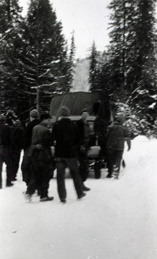 Several CCC enrollees surrounding the rear of a covered trucks on a snowy forest road in winter.