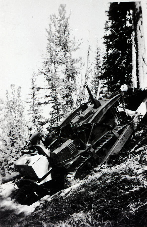 A CCC man drives a bulldozer up an incline pushing logs from the road.