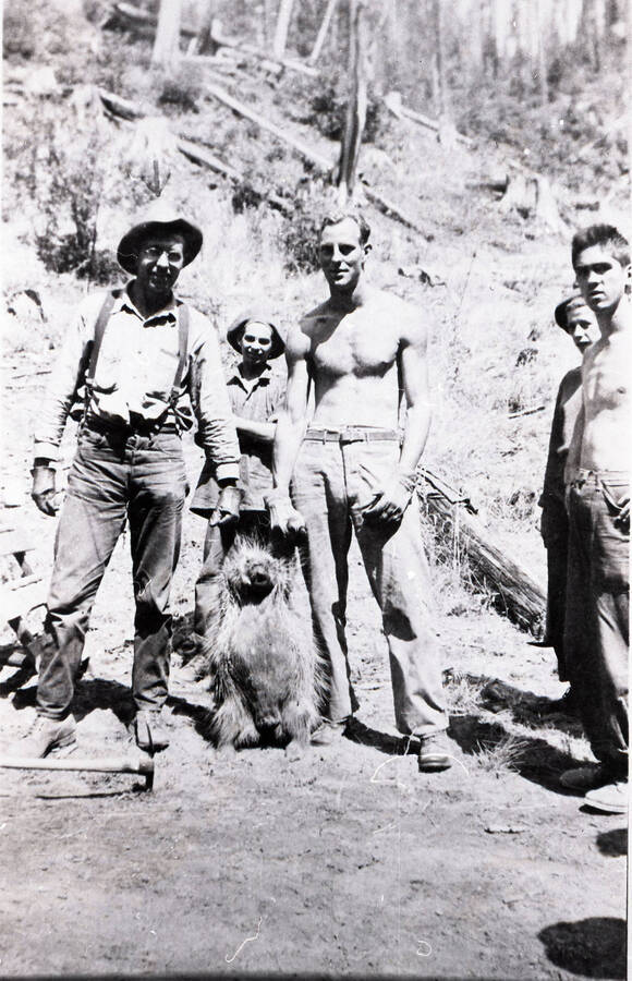 Five CCC men are pictured. Two of them hold a dead porcupine in gloved hands.