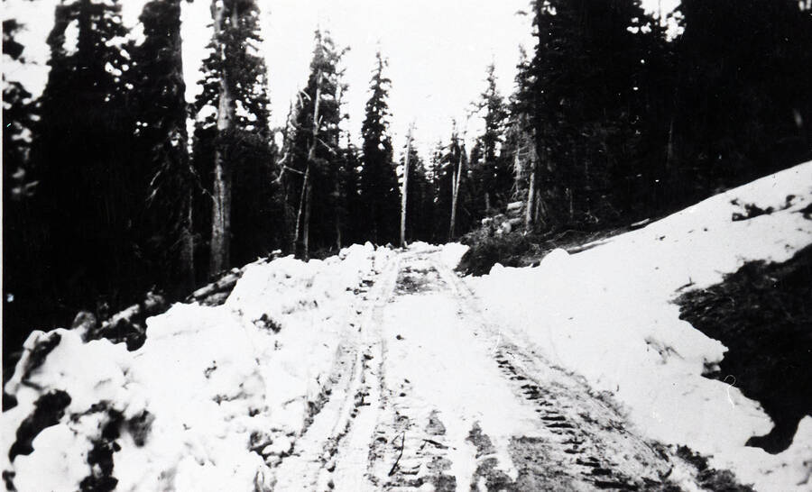 Photo of a road in winter, with bulldozer tracks in the snow.