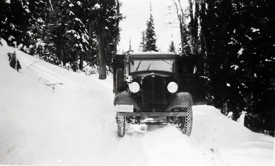 A CCC man poses for a photo, leaning out of the drivers side door of a truck on a snowy road. The truck's license plate reads: '15883'.
