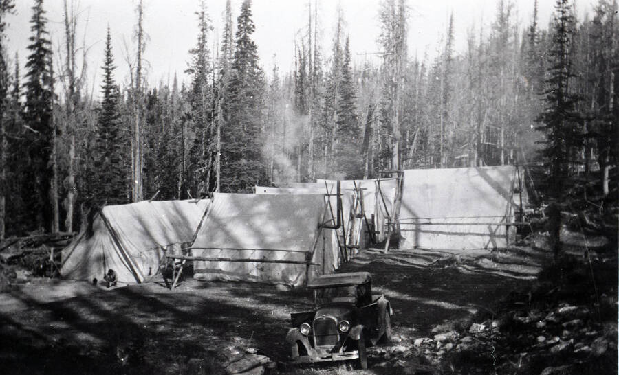 View of a rough tent camp with pickup truck parked in the foreground. A man sits outside the tent furthest to the left.