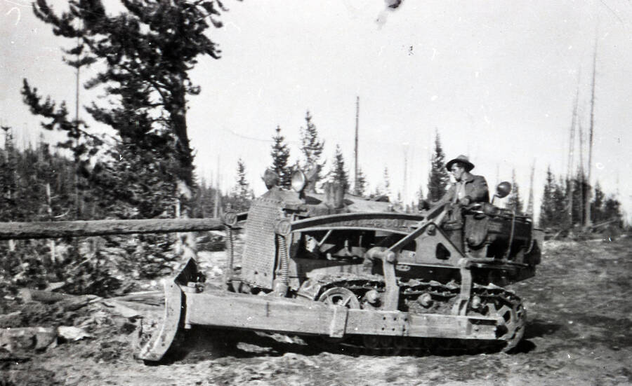 A CCC man drives a bulldozer in a logged clearing.