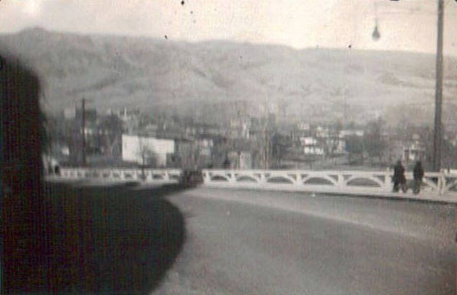 View of town across the road. Two pedestrians stand across the road. Writing under the photo reads: 'Lewiston, Idaho'.