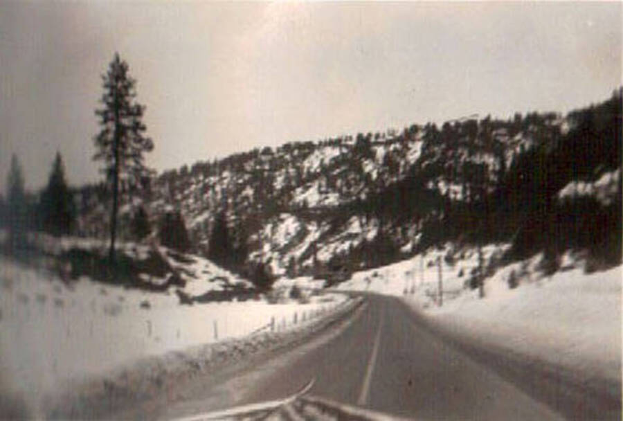 A road curves in the distance of a snowy and hilly landscape. Writing under the photo reads: 'Cascade Mt'.