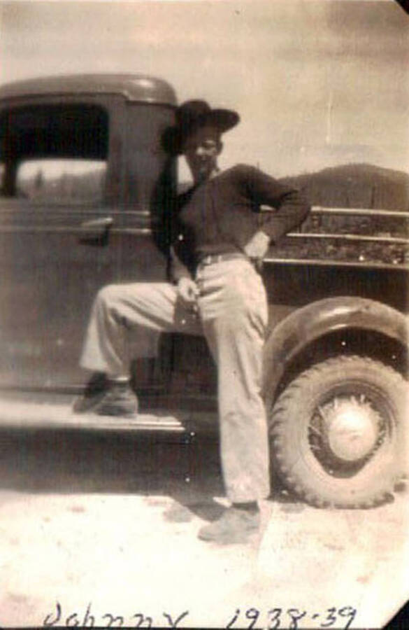 A CCC man wearing a cowboy hat leaning against a truck on a road. Writing on the photo reads: 'Johnny 1938-39'.